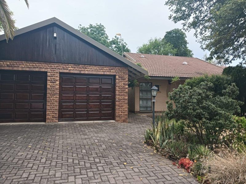 Front view of a residential property featuring a double garage with dark wood doors, a paved driveway, and a well-maintained garden area.