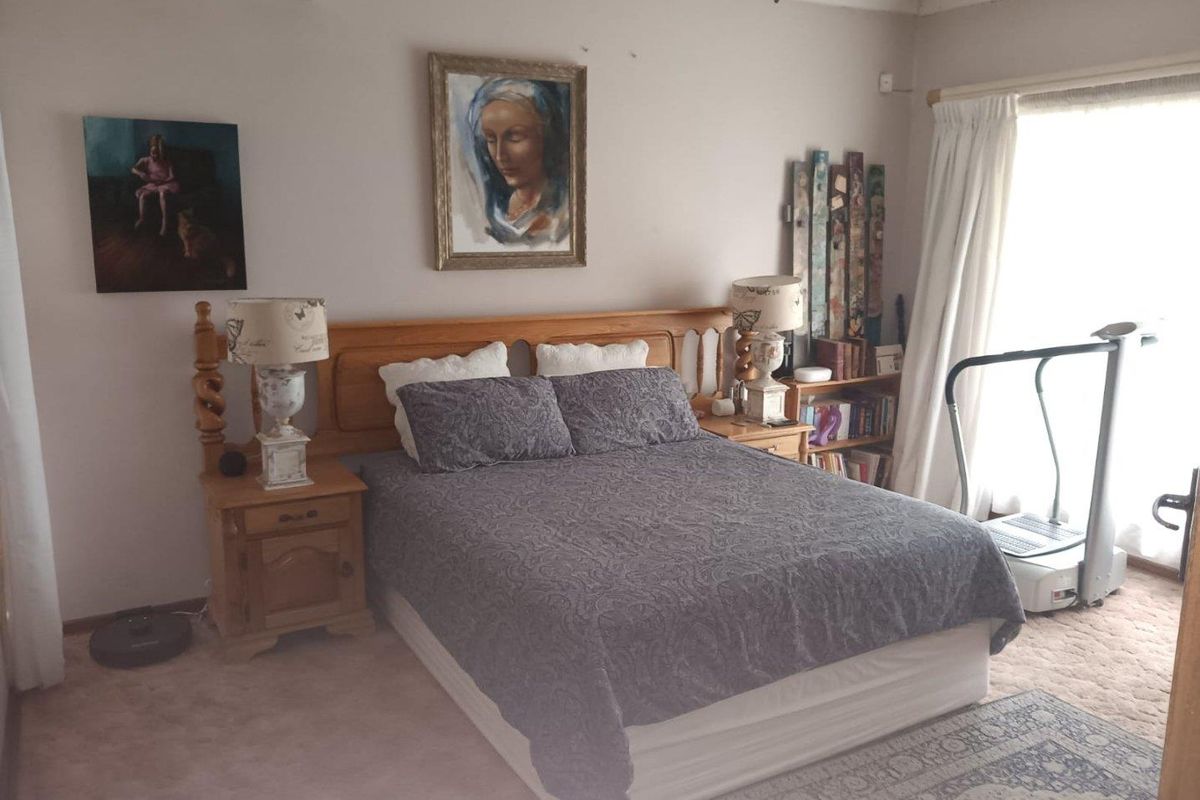 A carpeted bedroom featuring a wall-mounted air conditioning unit and natural light from a large window.