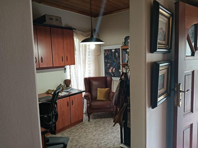 A compact home office featuring built-in wooden cabinetry, a timber-paneled ceiling, and a pendant light fixture, providing a functional workspace.