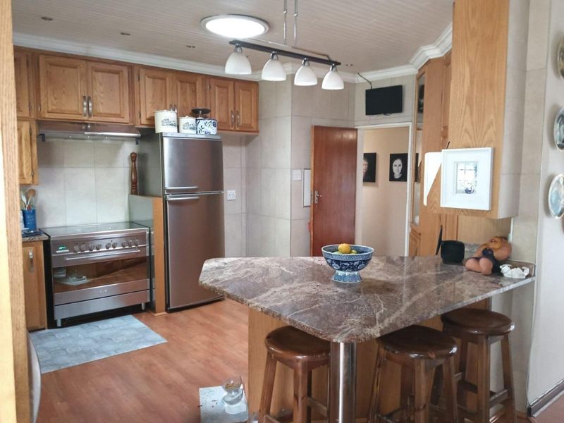 A functional kitchen featuring wooden cabinetry, stone countertops, a breakfast bar, and stainless steel appliances, with a tiled backsplash and laminate flooring.