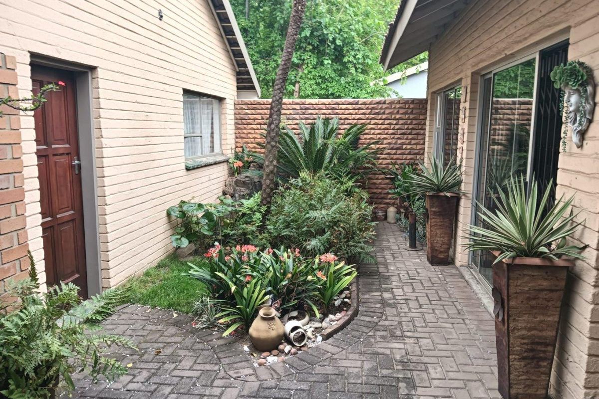 A private rear courtyard featuring brick paving, established garden beds, and access to the home via sliding glass doors and a side entrance.