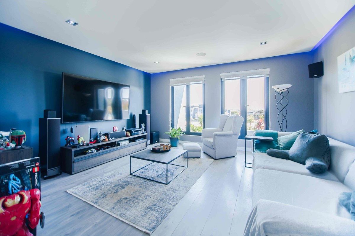 Modern living room featuring light wood-look flooring, recessed ceiling lighting, and large windows providing natural light.