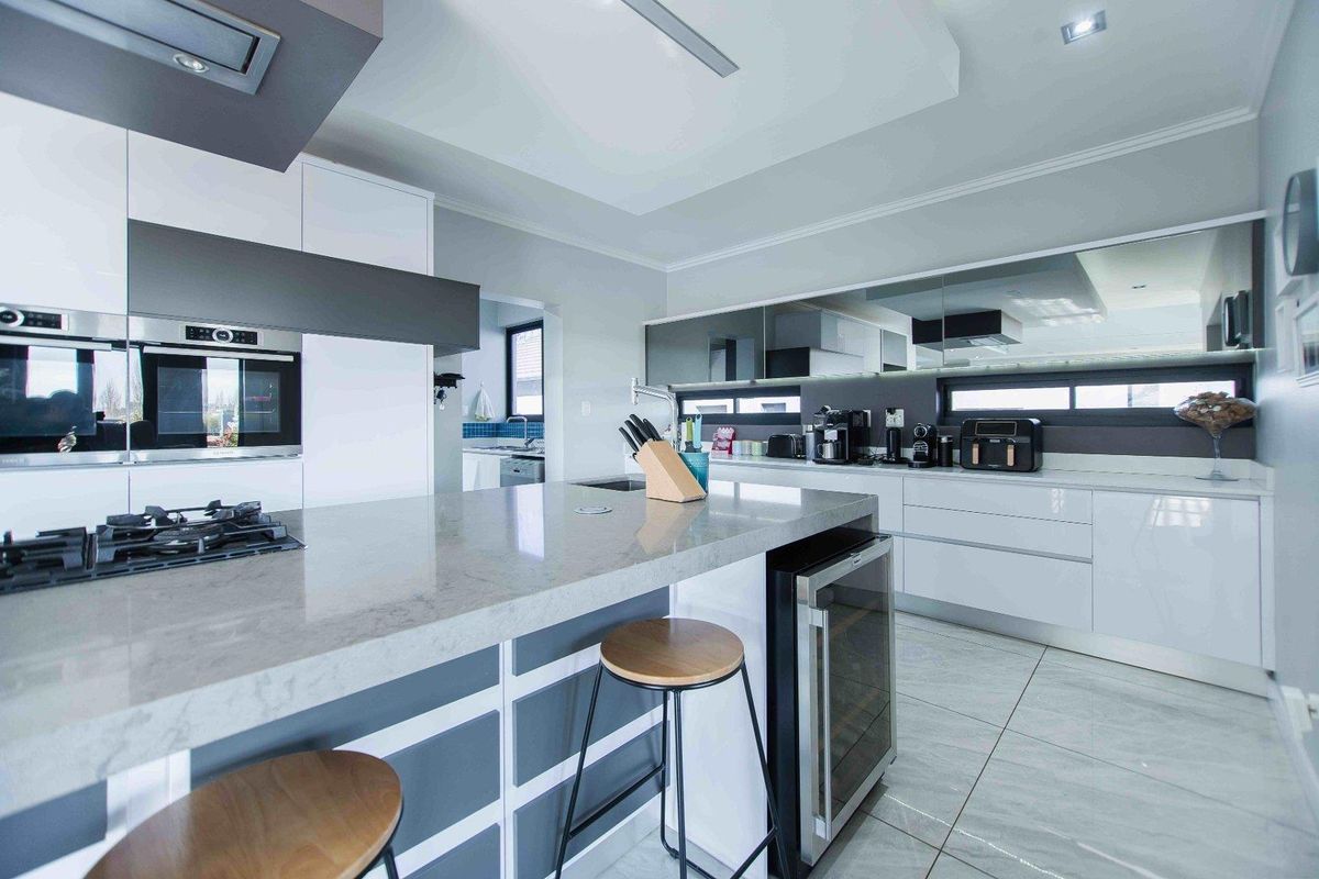 Modern kitchen featuring high-gloss cabinetry, stone countertops, a central island with a built-in wine cooler, and integrated stainless steel appliances.