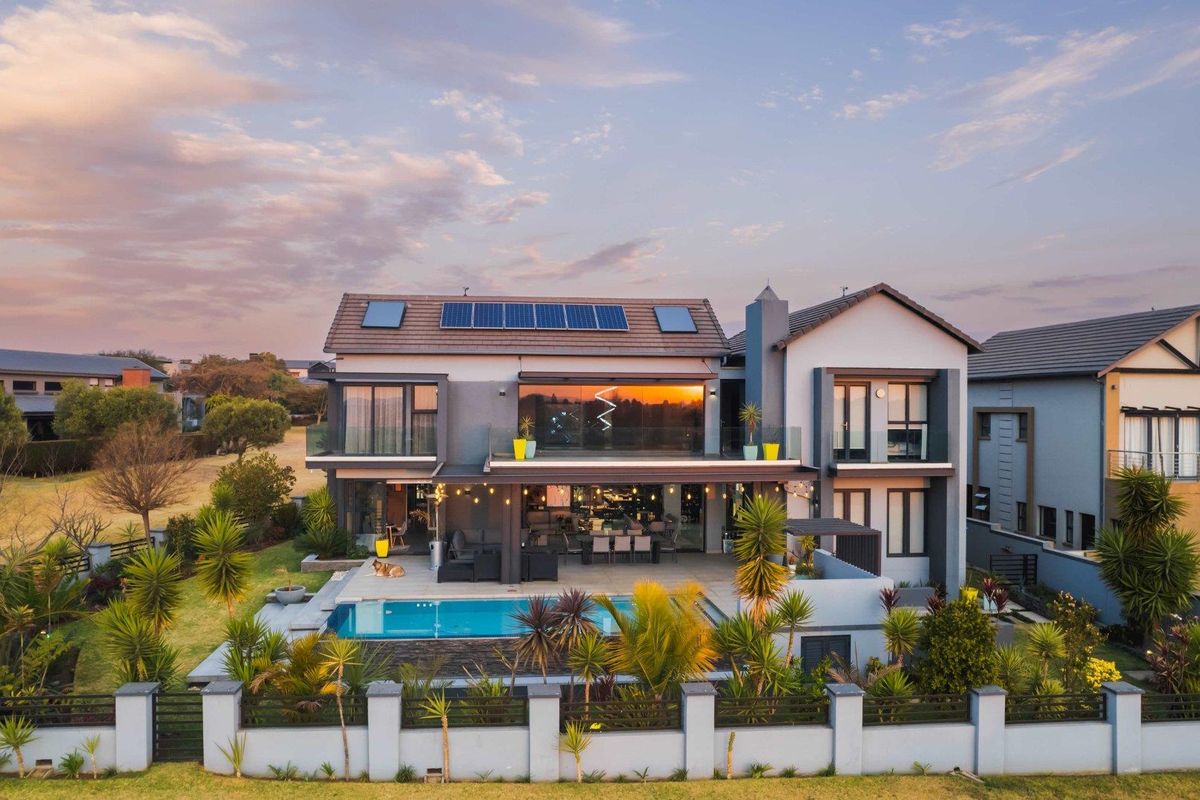 Aerial view of a modern double-story residence featuring a swimming pool, landscaped garden, solar panels, and a spacious covered patio area.