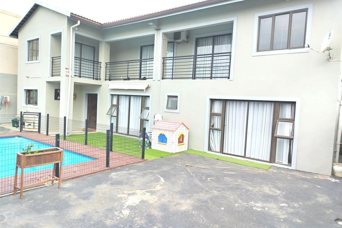 Rear view of a two-story house featuring a swimming pool, paved driveway, and multiple balconies with metal railings.