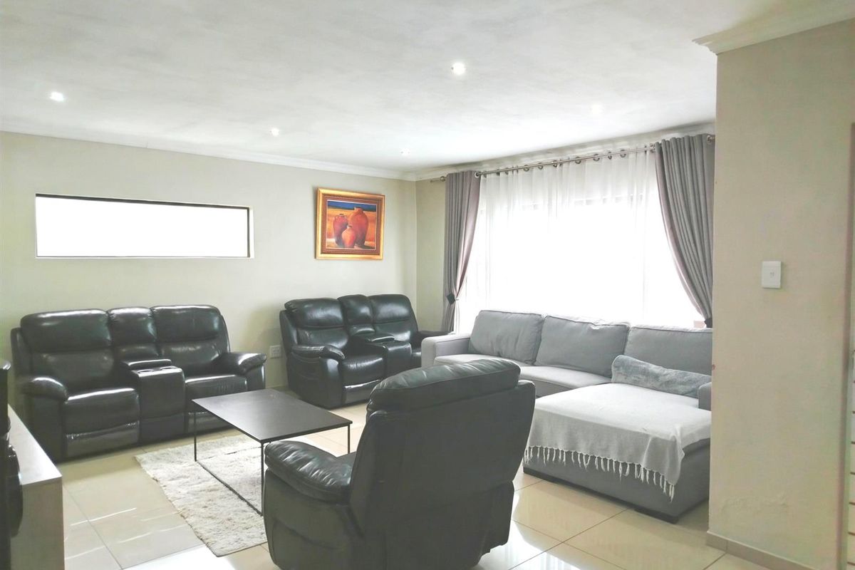 A spacious living room featuring neutral tiled flooring, recessed downlighting, and large windows allowing for ample natural light.