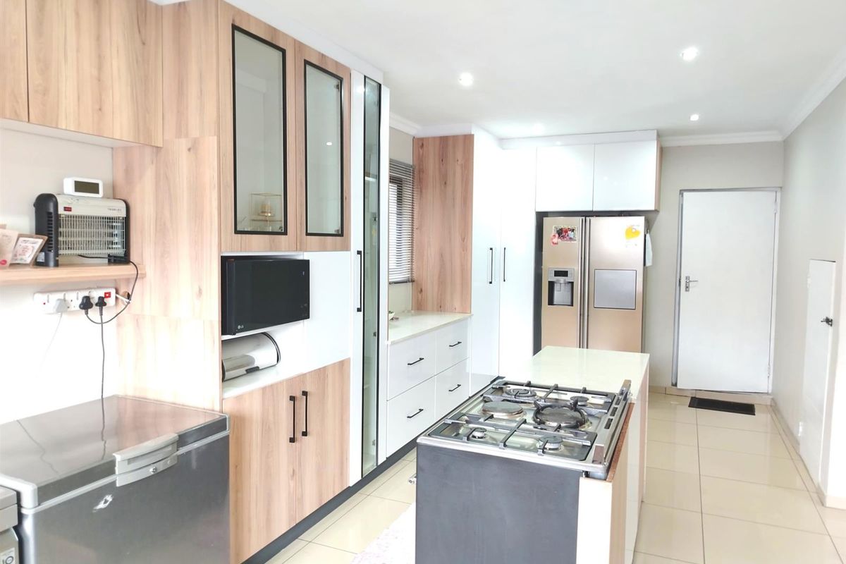 Modern kitchen featuring light wood-tone cabinetry, a central island with a gas hob, tiled flooring, and integrated storage solutions.