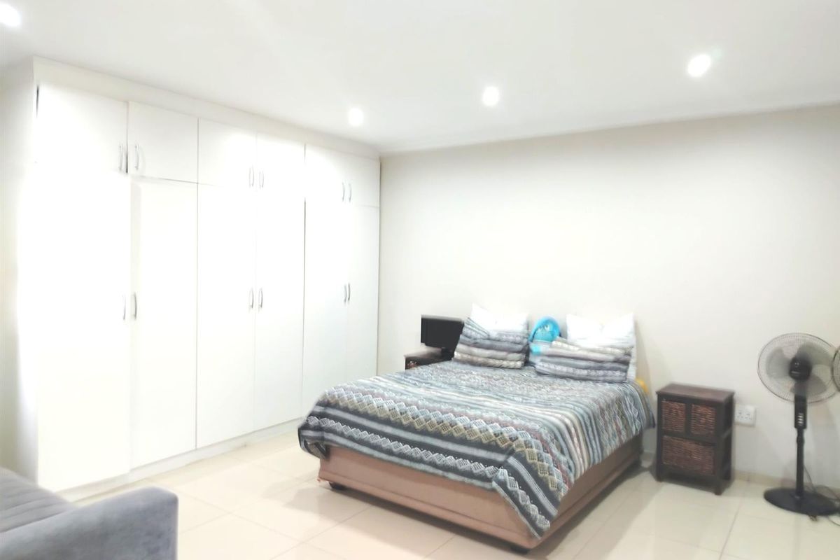 A spacious bedroom featuring neutral tiled flooring, recessed downlighting, and extensive built-in cupboard storage.