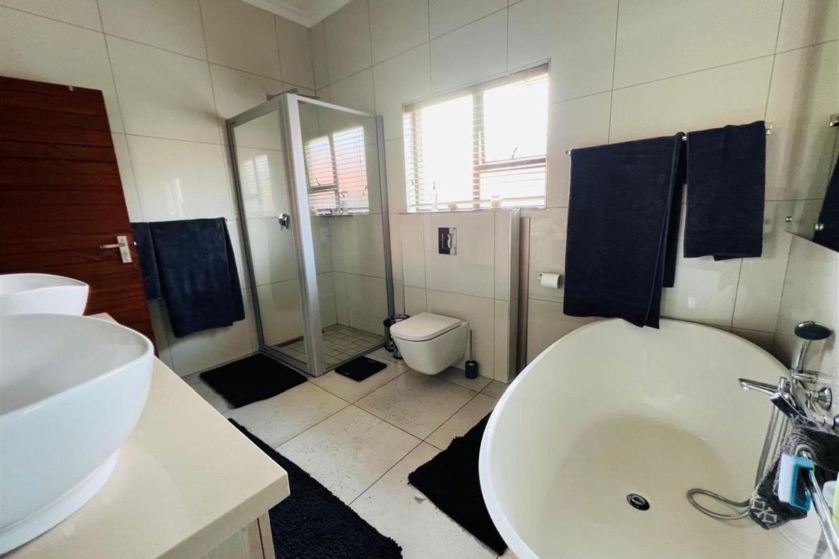Modern bathroom featuring a freestanding bathtub, glass-enclosed shower, wall-mounted toilet, and dual vessel sinks on a vanity unit with full-height wall tiling.
