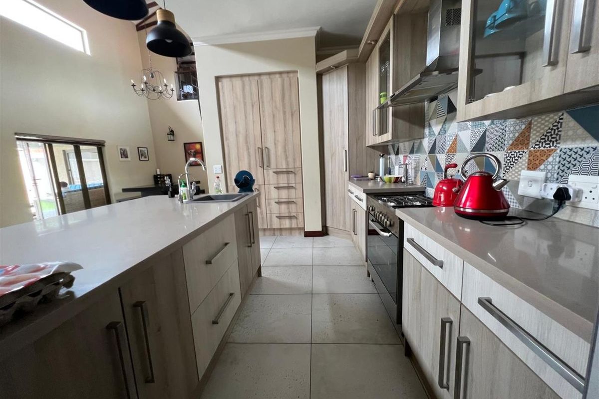 Modern open-plan kitchen featuring light wood cabinetry, stone countertops, a central island with a sink, and a decorative geometric tiled backsplash.