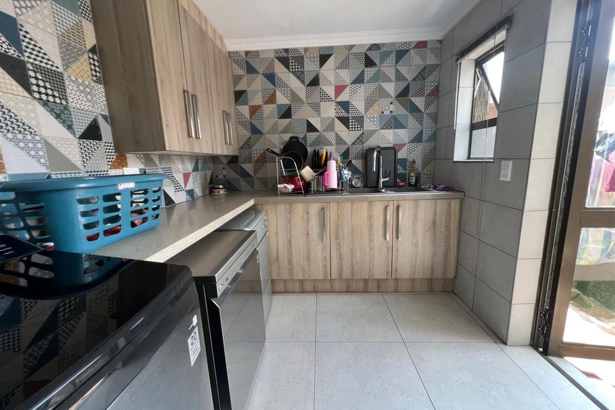 A functional laundry room featuring wood-look cabinetry, patterned tile splashbacks, tiled flooring, and dedicated plumbing connections for appliances.
