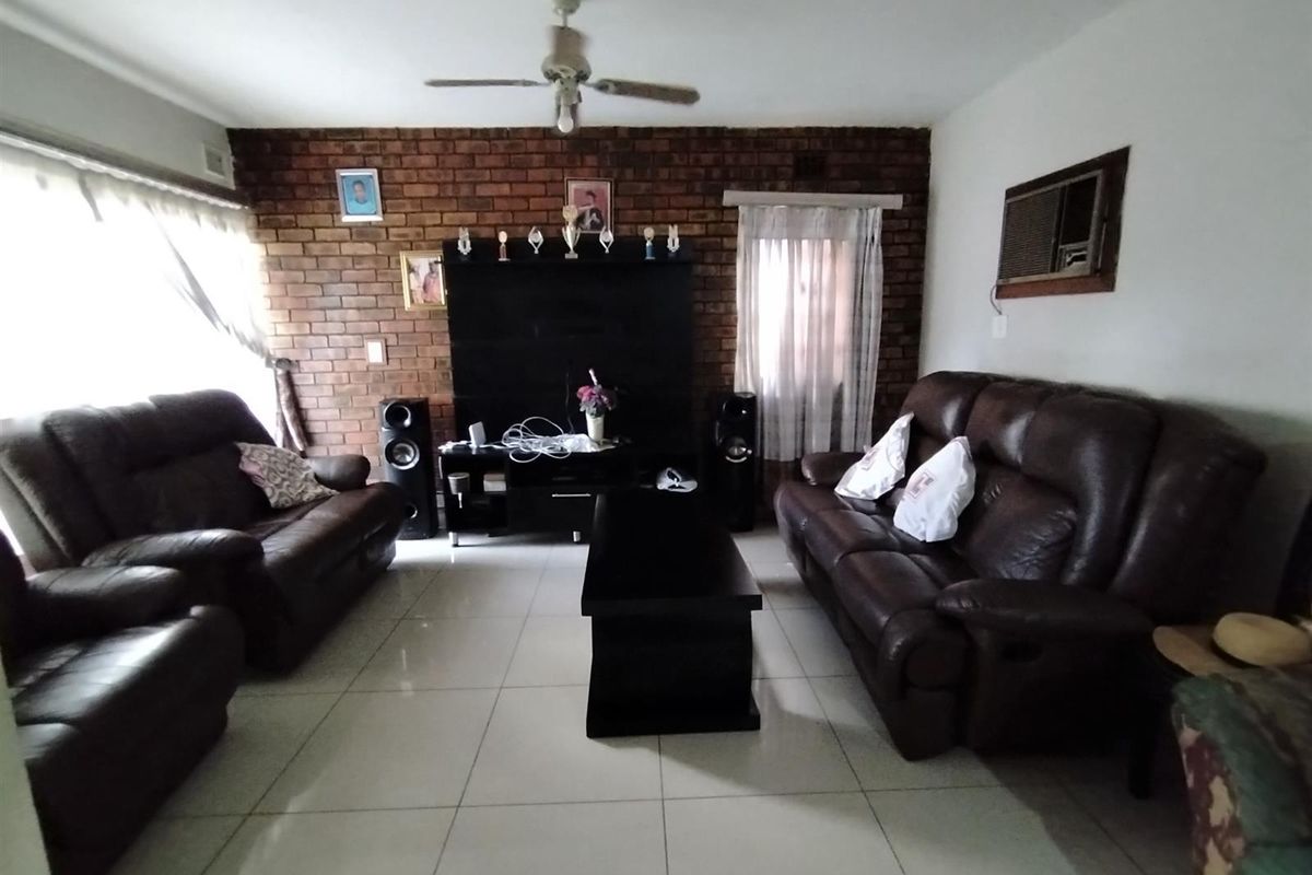 A living room featuring an exposed brick accent wall, tiled flooring, a ceiling fan, and a built-in window air conditioning unit.