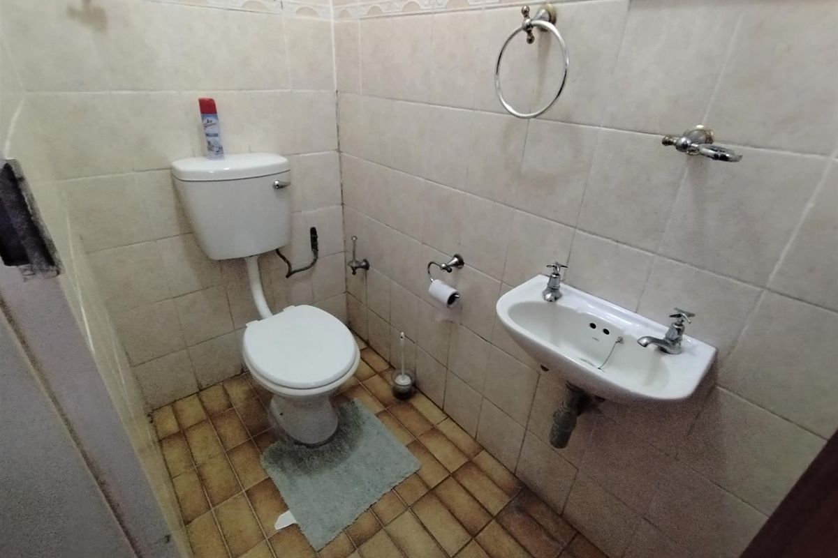 A compact guest bathroom featuring a wall-mounted basin and toilet, finished with dated wall and floor tiling.