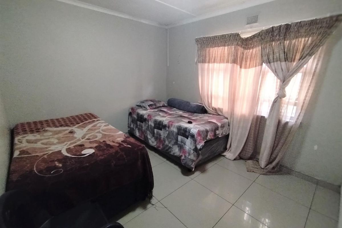 A functional bedroom featuring tiled flooring and a window with installed curtain rails, providing a neutral space ready for personalization.