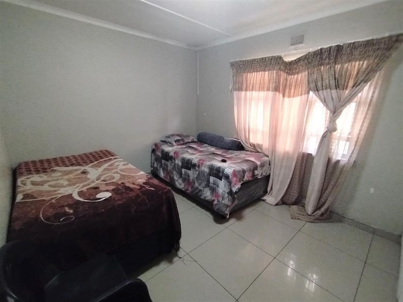 A functional bedroom featuring tiled flooring and a window with installed curtain rails, providing a neutral space ready for personalization.