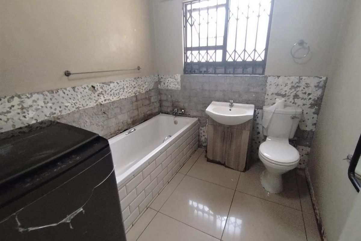 A bathroom featuring a bathtub, vanity basin, and toilet, currently requiring wall repairs and tiling to complete the finishes.