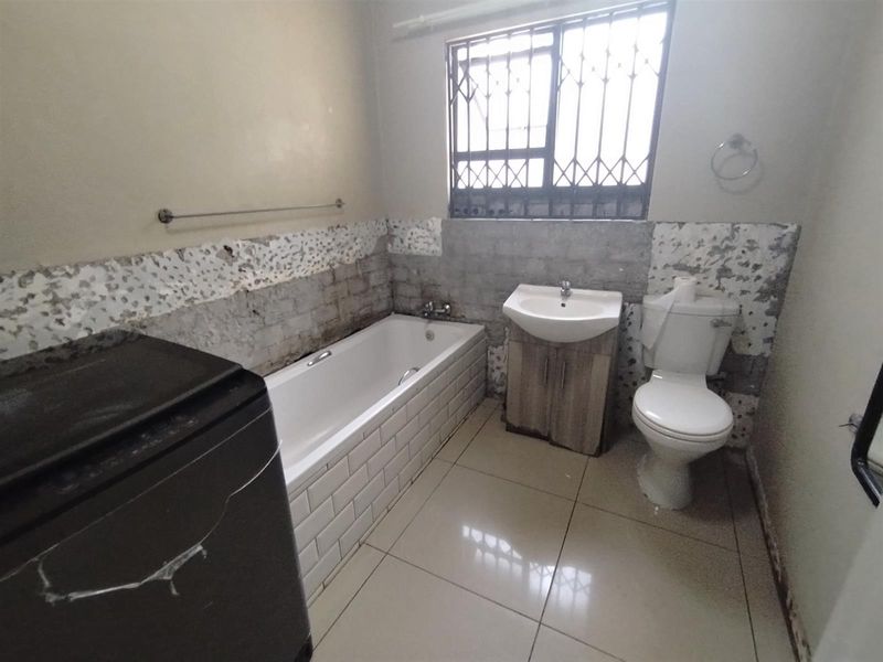 A bathroom featuring a bathtub, vanity basin, and toilet, currently requiring wall repairs and tiling to complete the finishes.