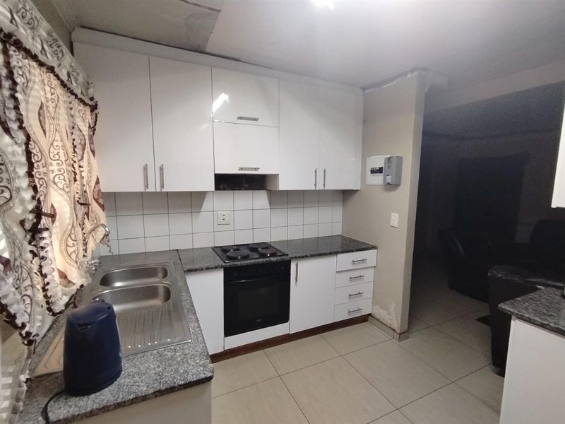 Compact kitchen featuring white cabinetry, granite countertops, built-in oven and hob, and tiled splashback, requiring some maintenance to wall finishes.