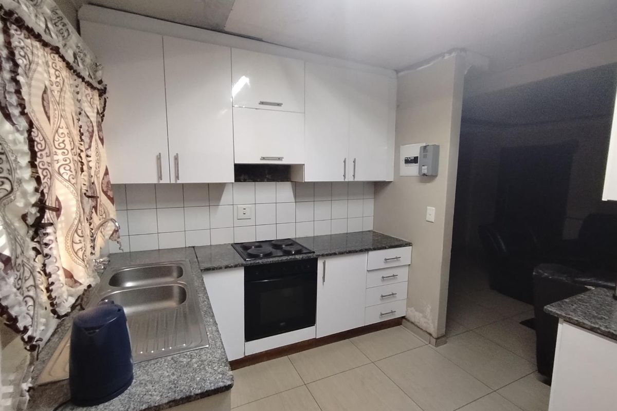 Compact kitchen featuring white cabinetry, granite countertops, built-in oven and hob, and tiled splashback, requiring some maintenance to wall finishes.