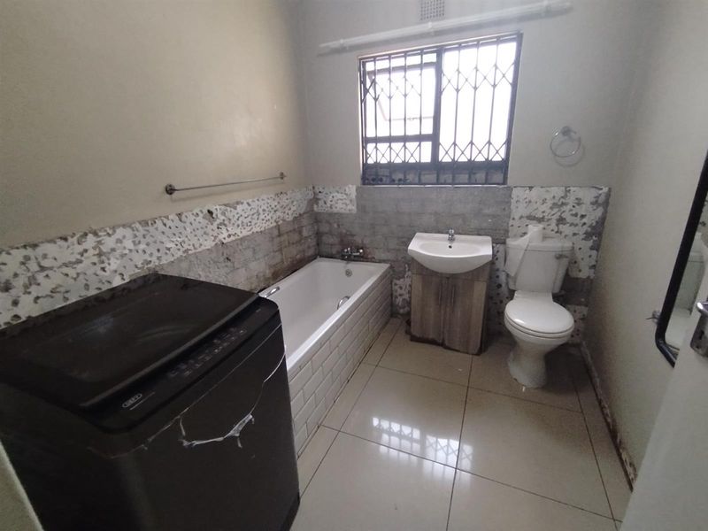 A bathroom featuring a bathtub, vanity basin, and toilet, currently requiring significant wall repairs and cosmetic renovation to restore its functionality and aesthetic appeal.