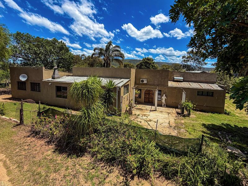 A single-story farm dwelling featuring a concrete patio area, metal roofing, and established garden surroundings in a rural landscape setting.