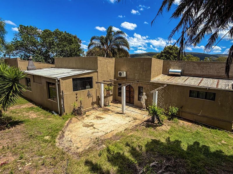 Rear view of the farm property featuring a concrete patio area, arched wooden entrance door, and corrugated metal roofing with solar water heating system.