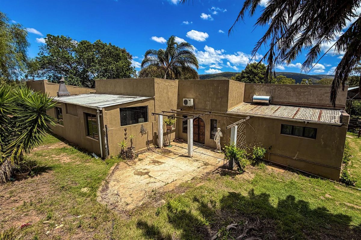 Rear view of the farm property featuring a concrete patio area, arched wooden entrance door, and corrugated metal roofing with solar water heating system.