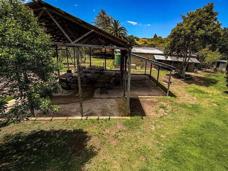 An open-air covered patio area with a timber frame structure, set within a spacious garden on the farm property.