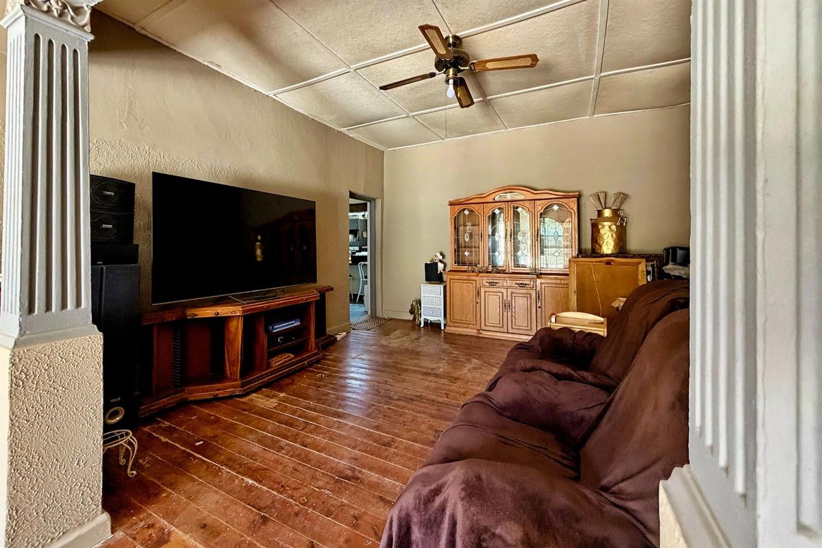 A living room featuring original timber flooring, a ceiling fan, and textured wall finishes, providing a rustic foundation for potential updates.