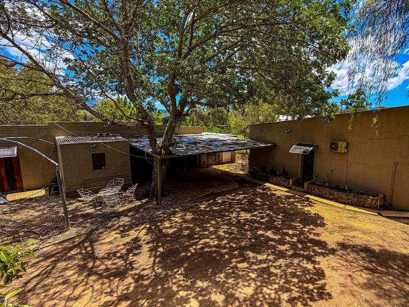 A rear exterior view of the farm property featuring a covered patio area, mature trees, and rustic building structures.