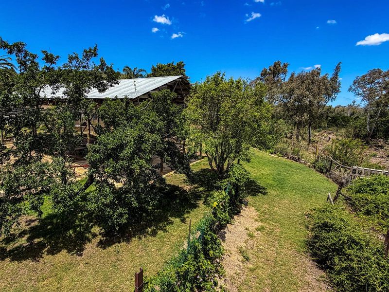 An elevated view of the farm property, showcasing the expansive garden area, mature trees, and the rear structure with a metal roof.