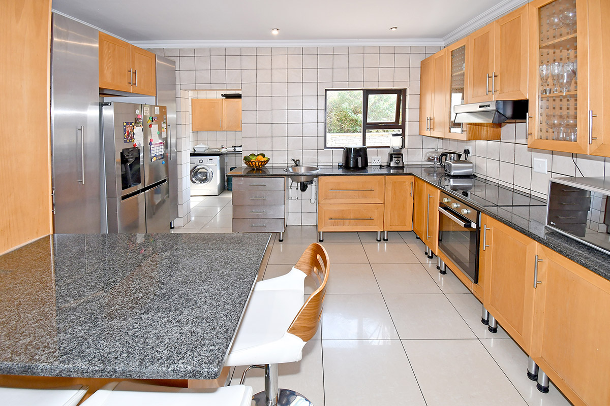 A functional kitchen featuring wooden cabinetry, granite countertops, built-in appliances, and a tiled backsplash, with an adjacent laundry area visible.