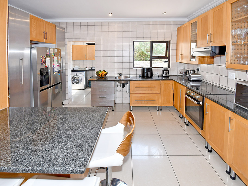 A functional kitchen featuring wooden cabinetry, granite countertops, built-in appliances, and a tiled backsplash, with an adjacent laundry area visible.