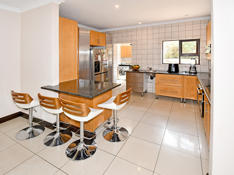Open-plan kitchen featuring wooden cabinetry, granite countertops, a central island with breakfast bar, and tiled flooring, with an adjacent laundry area.
