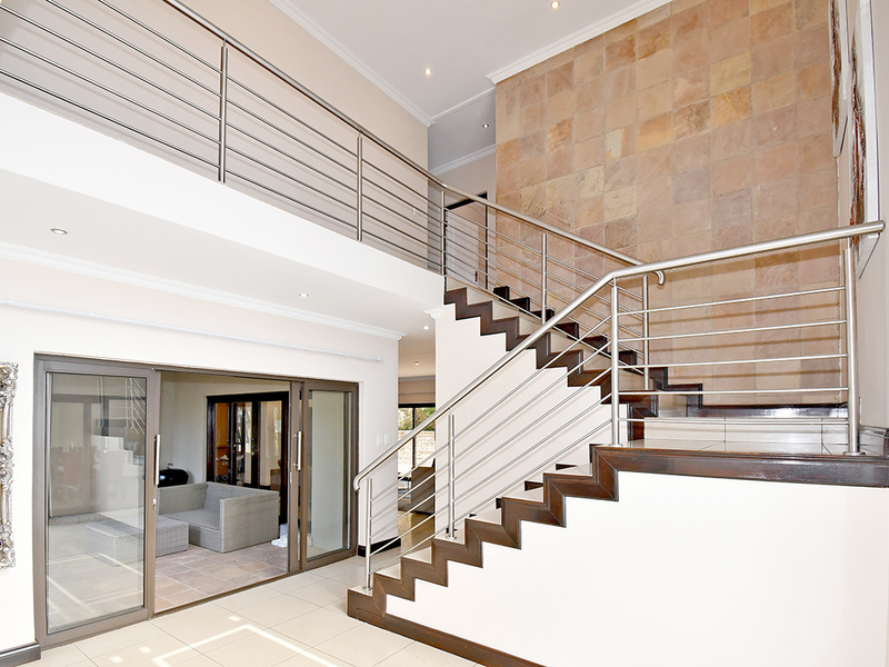 Spacious entrance hall featuring a striking stone feature wall, a modern wooden staircase with stainless steel balustrades, and large sliding doors leading to the patio.