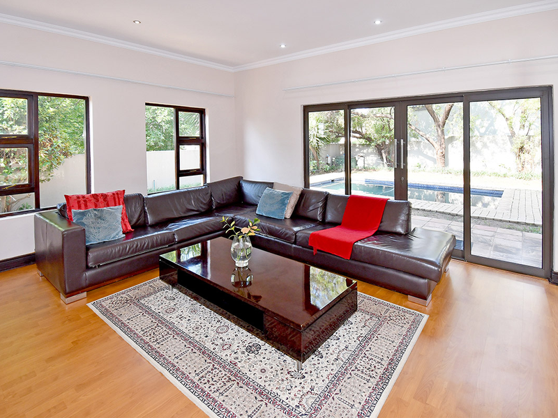 Spacious living room featuring laminate flooring, recessed lighting, and large sliding glass doors providing direct access to the outdoor pool area.