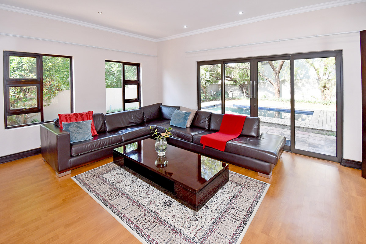 Spacious living room featuring laminate flooring, recessed lighting, and large sliding glass doors providing direct access to the outdoor pool area.