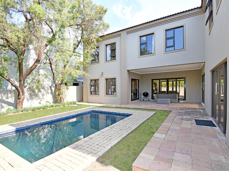 Rear exterior view featuring a swimming pool, paved patio area, and a two-story building facade with large aluminium-framed windows and sliding doors.