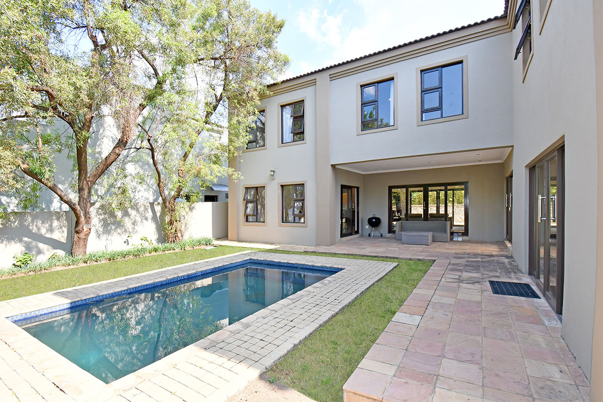 Rear exterior view featuring a swimming pool, paved patio area, and a two-story building facade with large aluminium-framed windows and sliding doors.