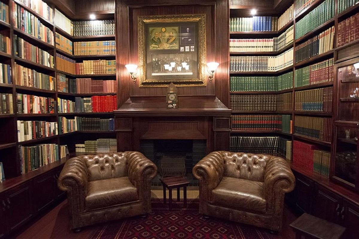 A sophisticated library room featuring extensive floor-to-ceiling custom wood cabinetry, built-in bookshelves, and a central fireplace with a decorative mantelpiece.