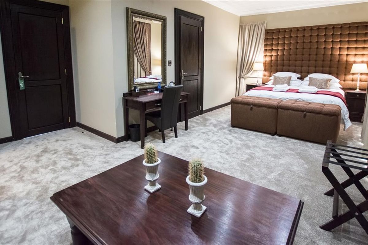 Spacious hotel bedroom featuring a large tufted headboard, plush carpeting, and dark wood doors, creating a comfortable and well-appointed guest suite.