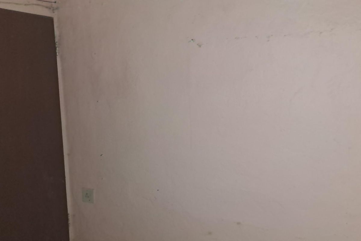 A plain, empty room featuring a standard interior door and a wall-mounted electrical socket, showing signs of wear and requiring cosmetic attention.
