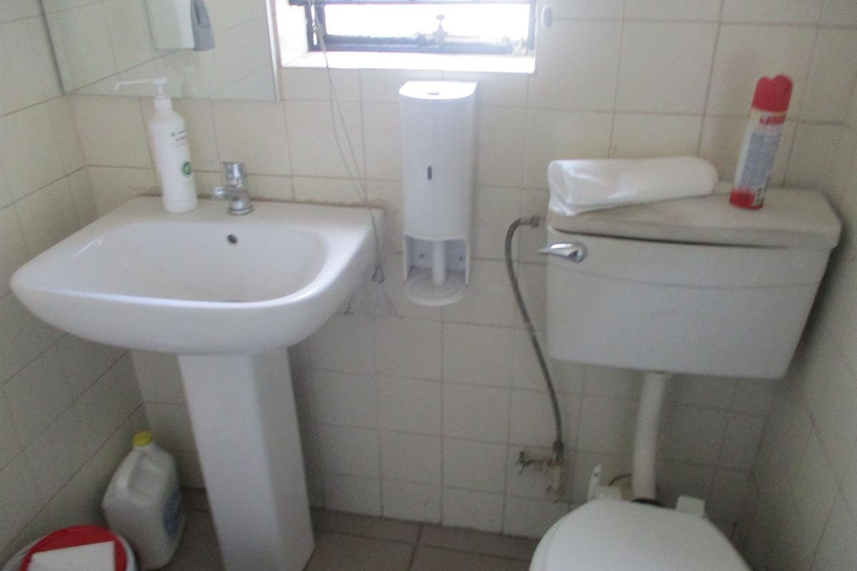 A compact commercial bathroom featuring a pedestal sink, standard toilet, and tiled walls with security bars on the window.