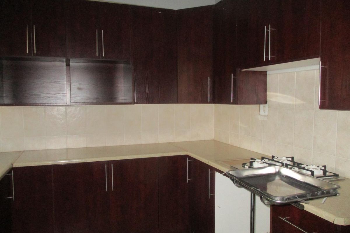 A kitchen featuring dark wood cabinetry, laminate countertops, and a tiled backsplash, currently requiring minor repairs to cabinetry and finishes.