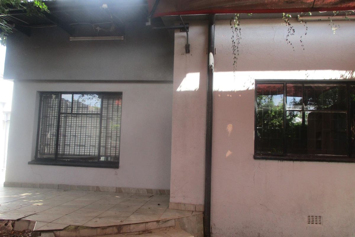 Rear exterior view of the commercial property featuring a tiled patio area, security-barred windows, and a shade cloth awning structure.