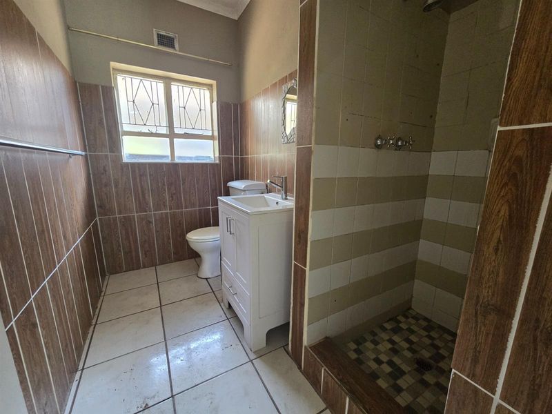 A functional bathroom featuring a shower enclosure, vanity basin, and toilet, finished with wood-look and striped wall tiling.