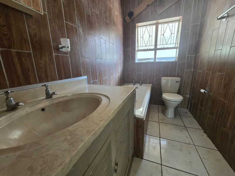 A dated bathroom featuring a built-in vanity, bathtub, and toilet with wood-look wall tiling and white floor tiles.