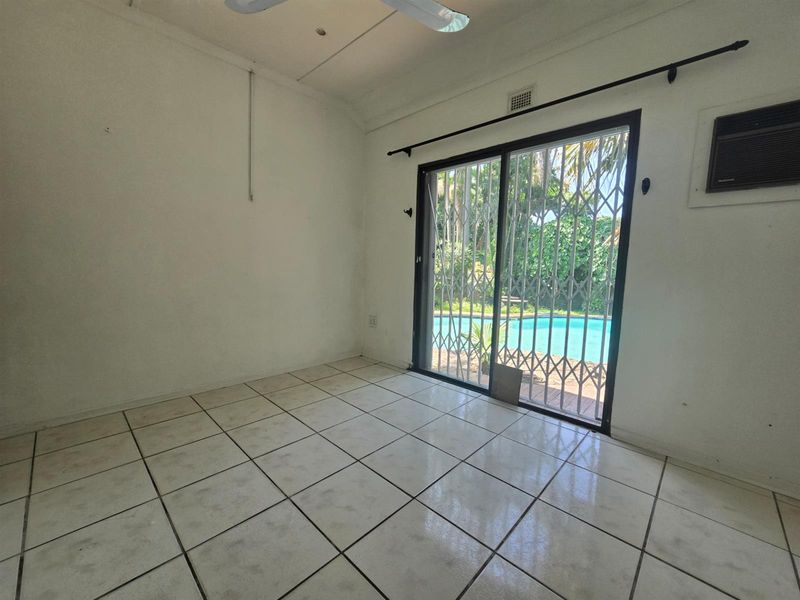 An empty living area featuring tiled flooring, a ceiling fan, and a sliding glass door with security gate providing direct access to the pool area.