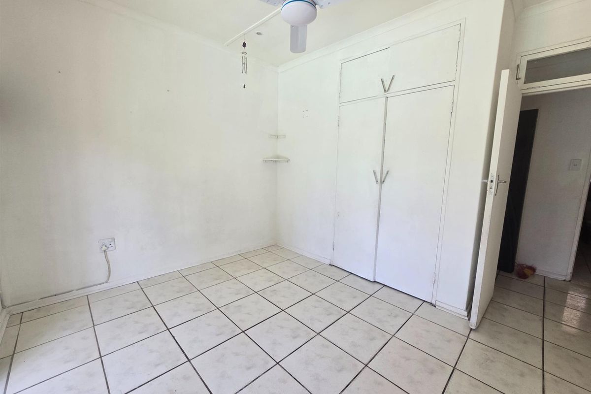 An empty bedroom featuring tiled flooring, built-in cupboards, and a ceiling fan, requiring cosmetic updates to the walls and flooring.