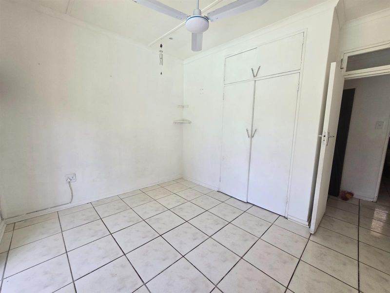 An empty bedroom featuring tiled flooring, built-in cupboards, and a ceiling fan, requiring cosmetic updates to the walls and flooring.